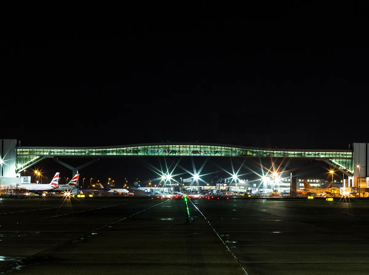 A night time image of an airport terminal bridge across the tarmac containing planes parked at their gates